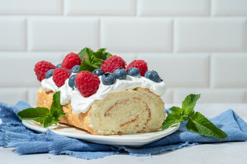 Sponge biscuit cake roll filling whipped cream and berries decorated raspberry, blueberry