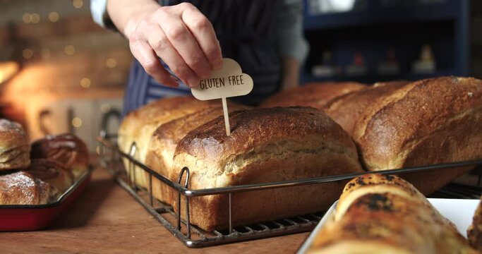 Sales Assistant In Bakery Putting Gluten Free Label Into Freshly Baked Baked Sourdough Loaves Of Bread
