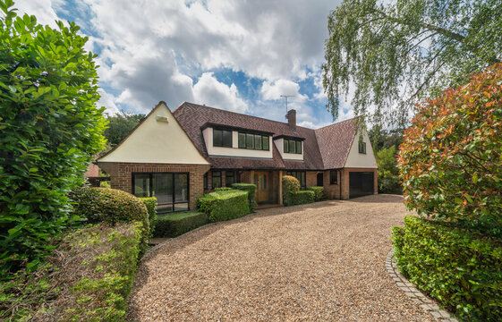 Luxury detached house in South East England with gravel drive and landscaped garden on summer day.
