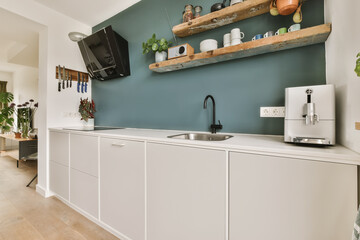 a kitchen with blue walls and white cupboards on the wall, there is a tv mounted above the sink