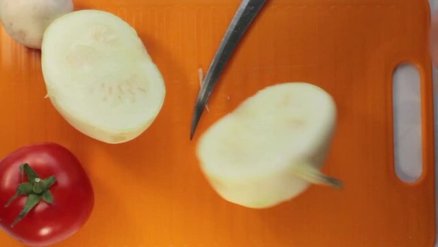 Closeup of a knife cutting a pattypan squash on an orange plastic board