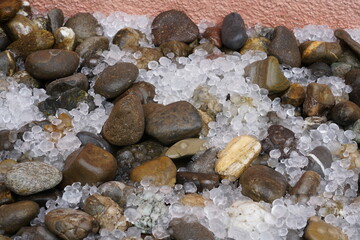 Hailstones spread on the ground with decorative stones.  It is a result of a heavy summer hailstorm. Suitable as a background for season, weather or meteorology related topics with some copy space.
