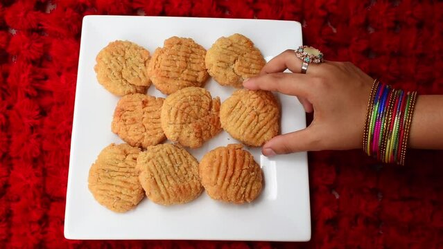 Thekua , an Indian sweet dish snacks in white plate . woman hand putting thekua on plate. Popular in bihar jharkhand. Prashad in chhath maha parv or puja or festival. selective focus.