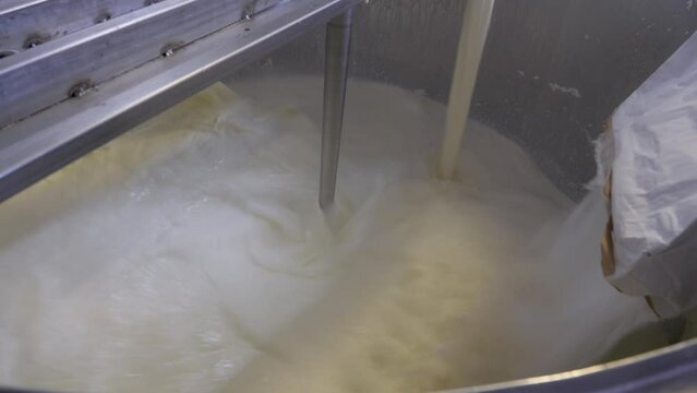 Adding dry ingredients from bag to metal tank of boiler where mixture is mixed with milk cream. Production of butter or ice cream at factory. Pasteurization and making of dairy products