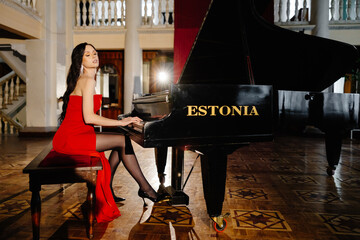 A luxurious actress in a red dress plays the piano in the great hall of the theater