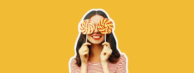 Portrait of cheerful smiling young woman covering her eyes with lollipop on yellow background