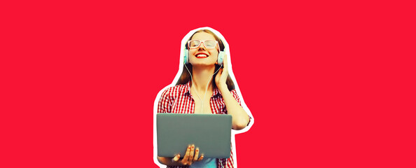 Portrait of modern young woman working with laptop listening to music in headphones on red background