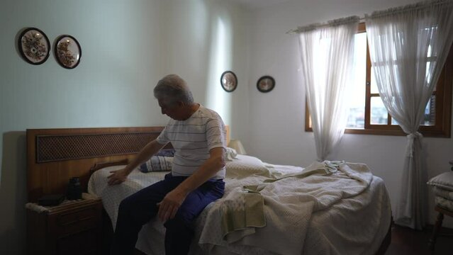 Senior man sitting on bedside, authentic real life portrait of elderly gray-hair person in casual bedroom, lifestyle scene depicting old age retirement