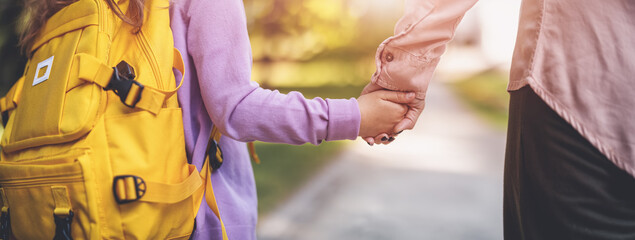 Mother holding the hand of a daughter and escorting her to school. - 626900382