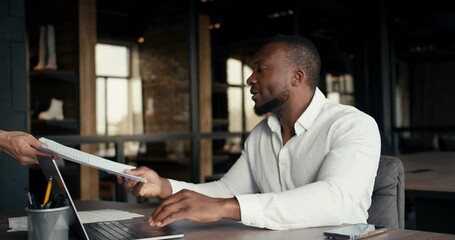 A Black man in a white shirt is brought a report on the work done in the office. Joy of success in fulfilling all plans and solving tasks