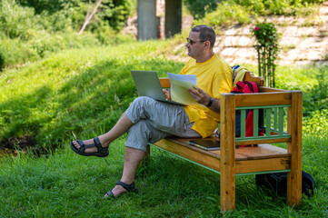 middle aged man with laptop and documents working outside in garden, green home office concept.