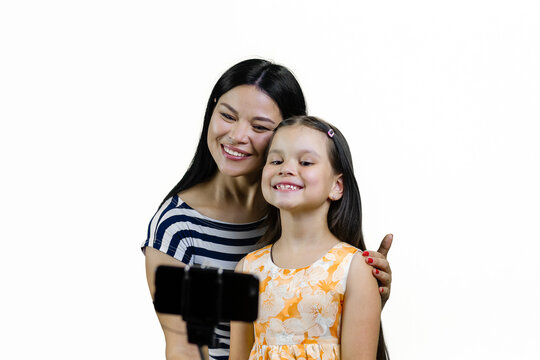 Young asian mother and her daughter taking selfie on smartphone using a selfie stick. Isolated on white.