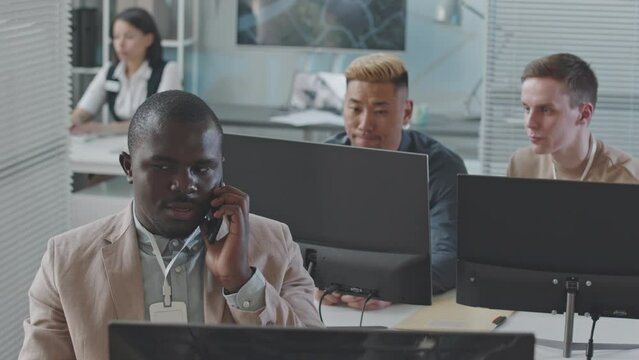 Slowmo of multiethnic team of data engineers working together in security agency, monitoring info on computers and making phone calls