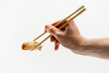 Close-up of a man's hand with chopsticks holding one eel sushi in the air on a white background 