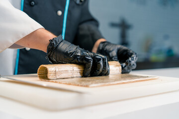 Close-up of a sushi maker in black gloves preparing sushi using rice nori sheets salmon fillet curd...