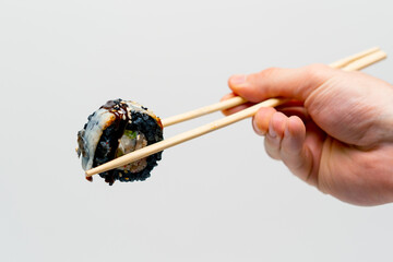 Close-up of sushi california with black rice and eel that a man holds with chopsticks on a white background