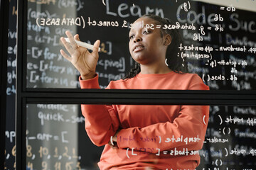 African American teacher standing near the glass board and explaining computer codes at lesson