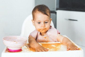 cheerful messy baby sits in a highchair and eats lure vegetable puree soup, the concept of baby food