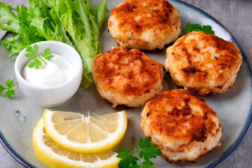 Cutlets with codfish and shrimps served with salad leaves, lemon and sour cream sauce on the plate