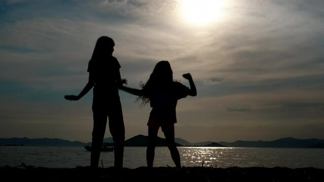 Children dance on the beach. Silhouette of little girls with long hair dancing on the beach.