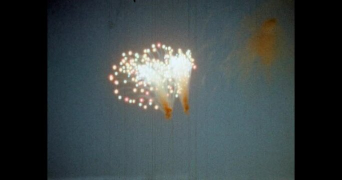 People crowd watching fireworks on city buildings background at night. Bright fireworks explode in blue sky. Holiday celebration at event. Archival vintage color film. Archive video. Old retro 1980s 