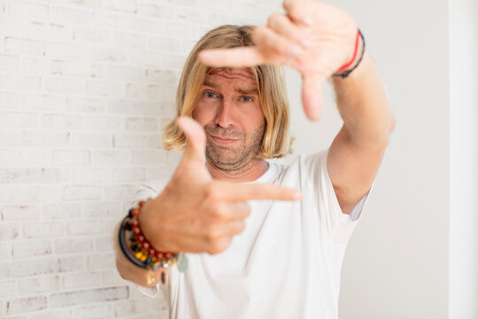 young blond adult man feeling happy, friendly and positive, smiling and making a portrait or photo frame with hands
