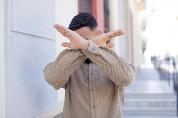 young handsome man covering face with hand and putting other hand up front to stop camera, refusing...