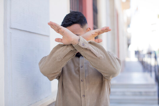 young handsome man covering face with hand and putting other hand up front to stop camera, refusing photos or pictures