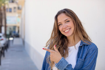 pretty hispanic woman smiling cheerfully, feeling happy and pointing to the side and upwards, showing object in copy space