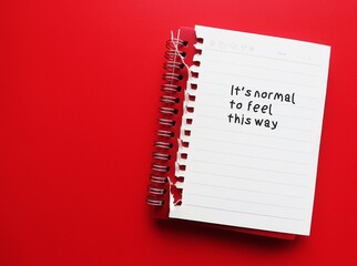 Notebook on red copy space background with handwritten text - It’s normal to feel this way - self...