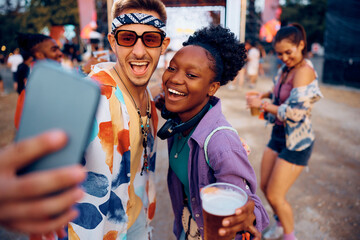Cheerful couple of festival goers taking selfie with cell phone.