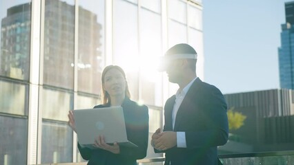 Two business partners man in virtual reality glasses and woman with laptop in hands, future VR presentation of new development project, office building rooftop terrace overlooking city downtown - Powered by Adobe