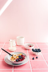 Gesundes Frühstück mit Joghurt, Haferflocken und frischen Beeren  in einer Schüssel. Rosa Kacheln, Tisch.