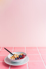 Eine Frühstück Schüssel mit Müsli, Joghurt und frischen Beeren auf rosa Kacheln. Minimalistisch.