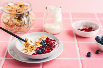 Eine Schüssel mit Müsli, Joghurt und frischen Beeren auf rosa Kacheln. Zutaten, Frühstück.