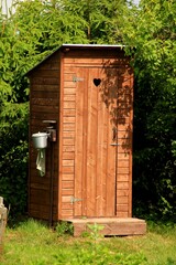 Brown wooden toilet in a country house near a green bush. Small wooden outdoor toilet