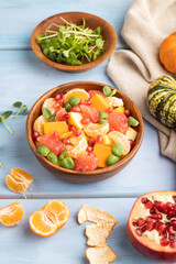 Vegetarian fruit salad of pumpkin, tangerine, pomegranate, microgreen sprouts on blue, side view, close up.