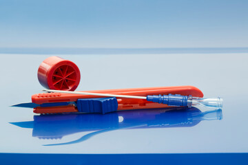 Red safety scalpel, filter needle and red locking disposal cup on blue background