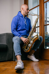 Naklejka premium vertical portrait of young venezuelan man playing saxophone at home