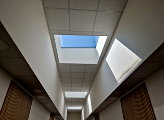 high above the head is a rectangular window illuminating the entire area of the hall with natural light. the window is a rectangular skylight. the walls are pure white plaster - obrazy, fototapety, plakaty