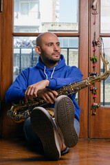 vertical portrait of young saxophonist sitting sleepily at home with his saxophone