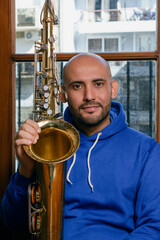 portrait of young latin man saxophonist sitting at home with his saxophone looking at the camera