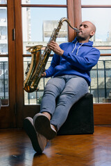 Naklejka premium young latin man sitting at home inspired and excited playing the saxophone.