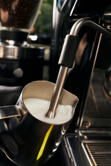 cropped view of barista frothing milk in pitcher, foaming milk, professional coffee machine, latte