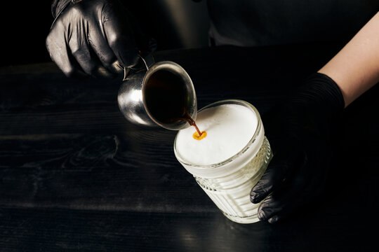 barista in latex gloves preparing latte macchiato, pouring espresso, pitcher with black coffee