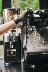 professional coffee machine, cropped view of barista in latex glove near steamer and coffee grinder
