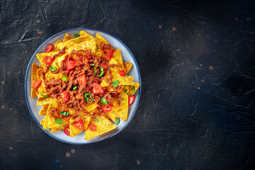 Nachos, Mexican food, tortilla chips with beef and fresh vegetables, shot from the top on a black slate background with copy space