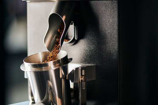 cafe equipment, ground coffee pouring from electric coffee grinder into measuring metallic cup