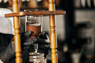 barista in black latex gloves assembling parts of cold drip coffee maker, alternative coffee brewing