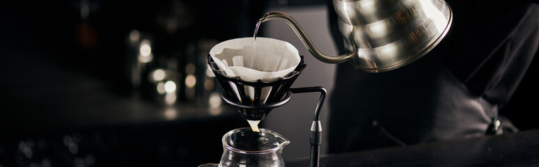 barista pouring boiling water into coffee filter on dripper stand above glass pot, V-60 style,...